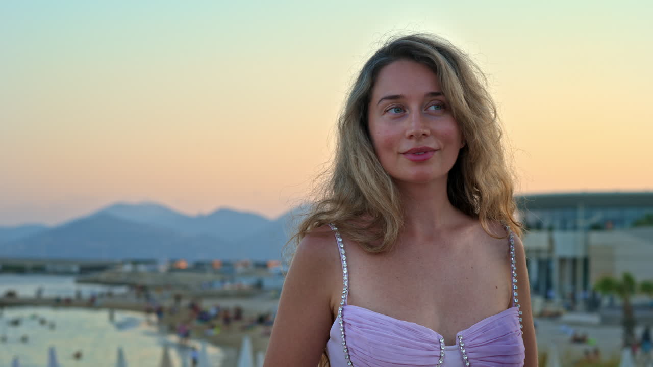 Woman in pink dress posing with the beach on the background in the evening in Cannes, France
