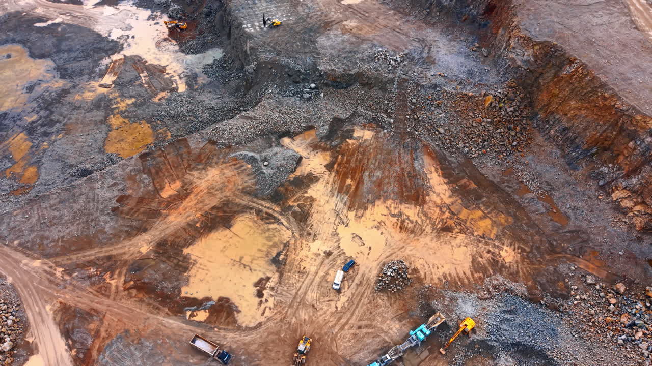 Heavy machinery at work in a mining site. Several machines operate in a large mining area during daylight. Trucks and excavators move soil and rocks around