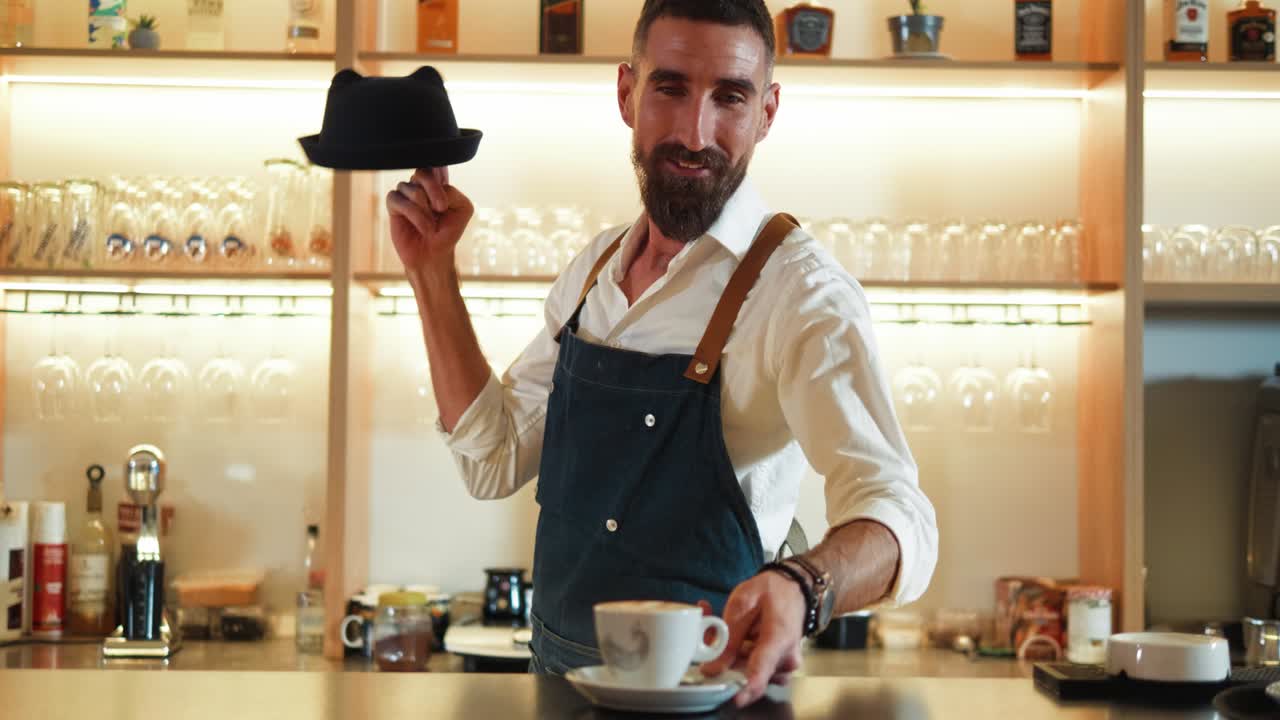 기쁜 남성 바리스타가 테이블 위에 커피 컵을 놓고 카메라를 바라보는 초상화