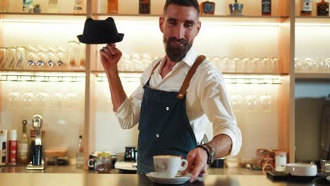 portrait of a cheerful male barista  putting coffee cup on the table and looks at the camera