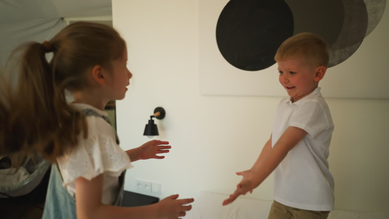 아이들은 호텔의 침대에 함께 뛰어다니며 기쁜 작은 형제는 침실에서 매트리스에 뛰어다니는 소녀의 손을 잡습니다.