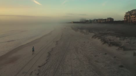 aerial, man running on the beach early in the morning, sea mist rolling inland