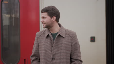 young man in trendy overcoat waiting on train station, looking around