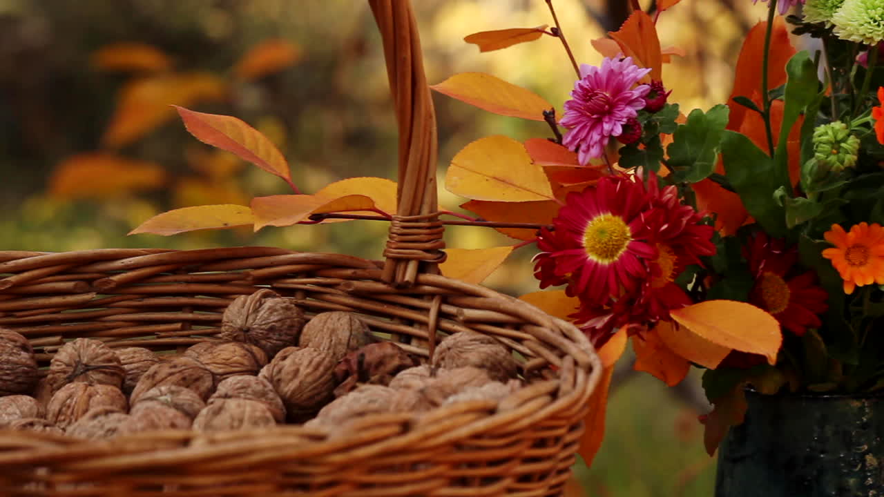 Cesto di vimini con noci accanto a un vaso di fiori all'aperto su un tavolo