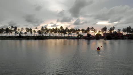 4k aerial fly by drone shot of a 28-year-old indian male kayaking in the backwaters of varkala during sunset, kerala