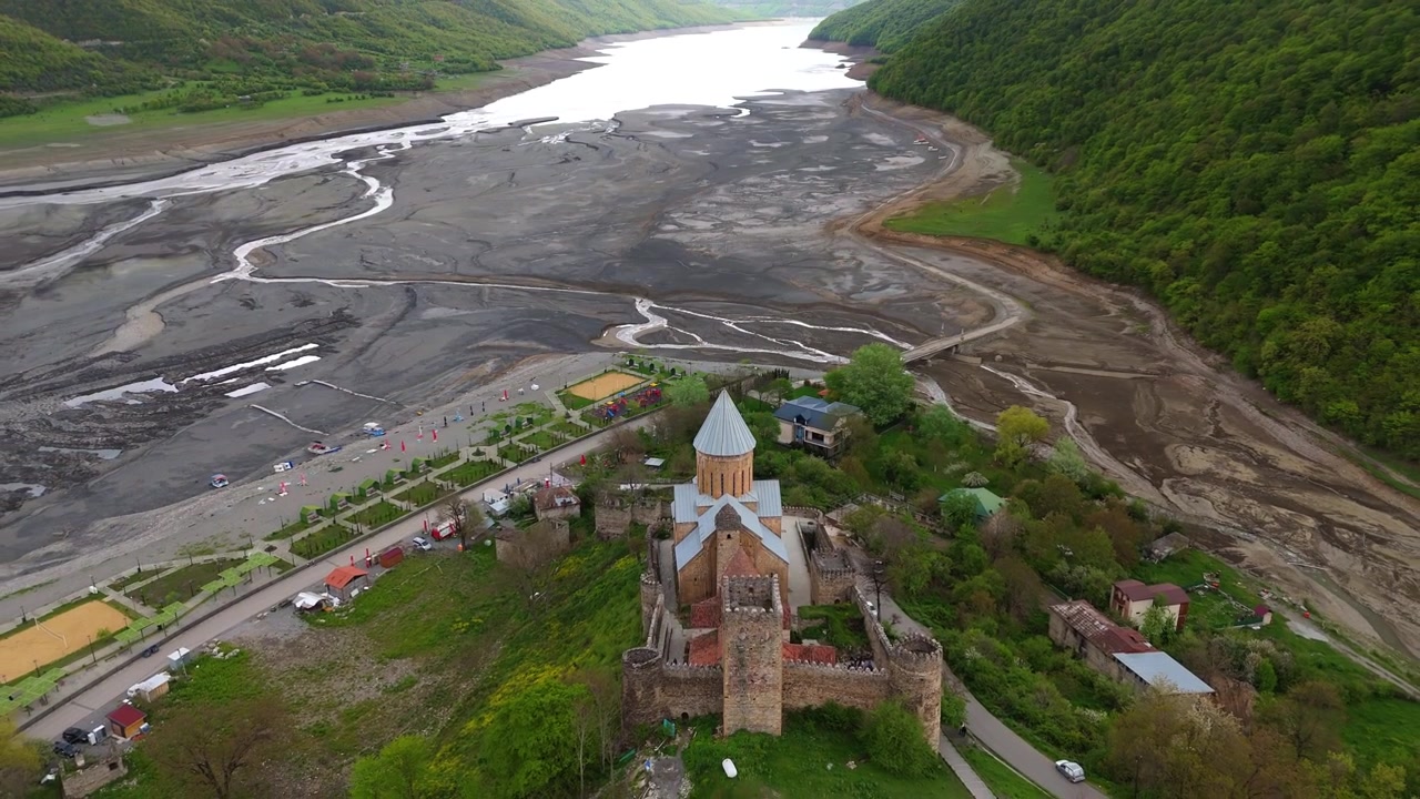 Letecký pohled na starobylé kamenné zdi a kónické střechy pevnosti Ananuri v Gruzii. Detailní pohled na středověkou gruzínskou architekturu a historické zdivo na pozadí dramatické oblohy.
