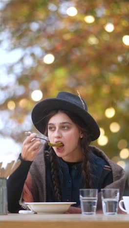 mujer joven comiendo sopa al aire libre en otoño
