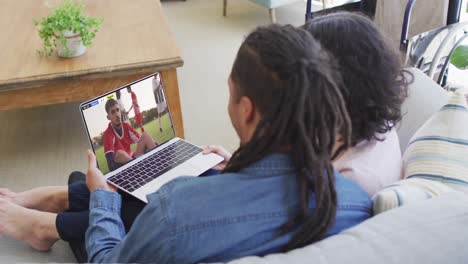 Biracial-couple-laptop-with-diverse-male-soccer-players-playing-match-on-screen
