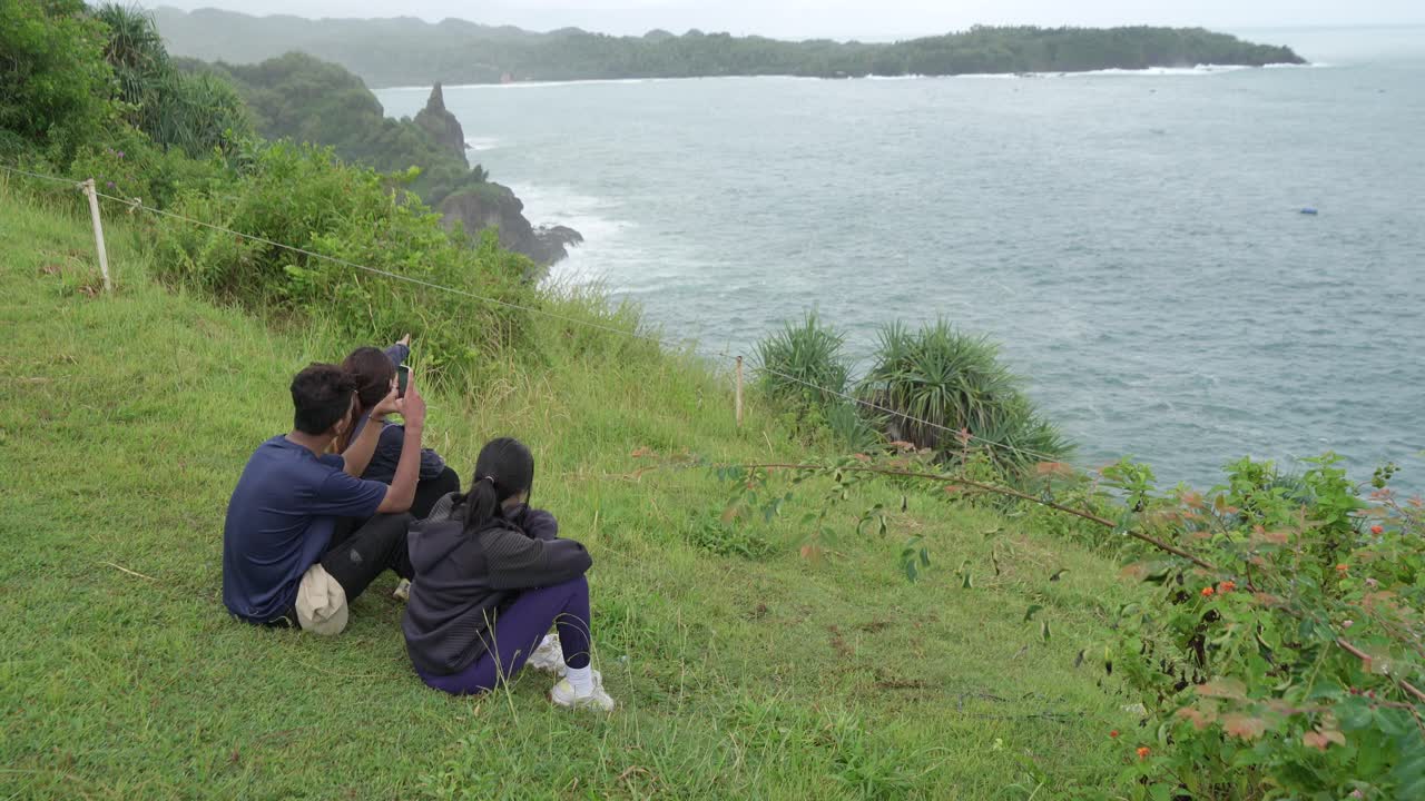 People taking pictures of the ocean view from a hilltop