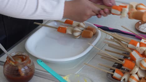 joven con delantal preparando suki satay en un plato para asar