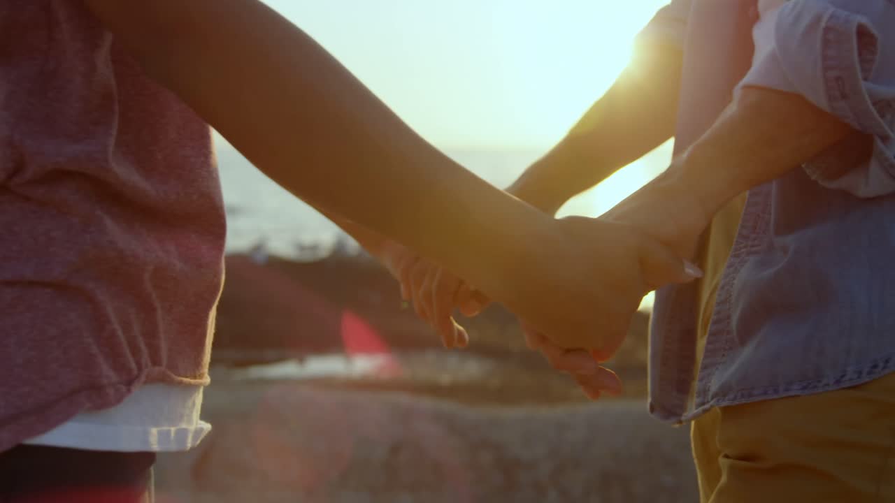 해변 4k에서 바위 위에 서 있는 동안 손을 잡고 있는 혼혈 커플의 중간 섹션