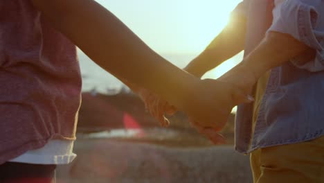 Mid-section-of-mixed-race-couple-holding-hands-while-standing-on-rock-at-beach-4k