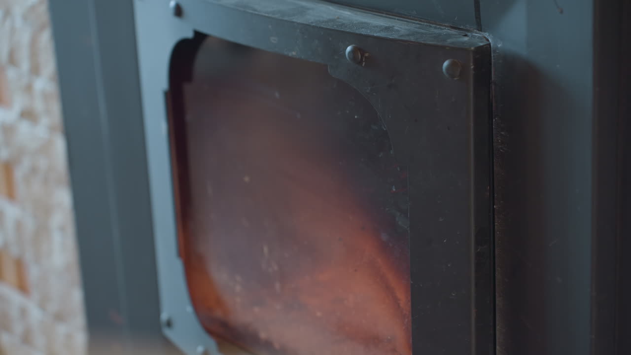 Close up of fireplace interior as door begins to close, partially revealing stacked wood catching fire inside, flames flicker gently in background