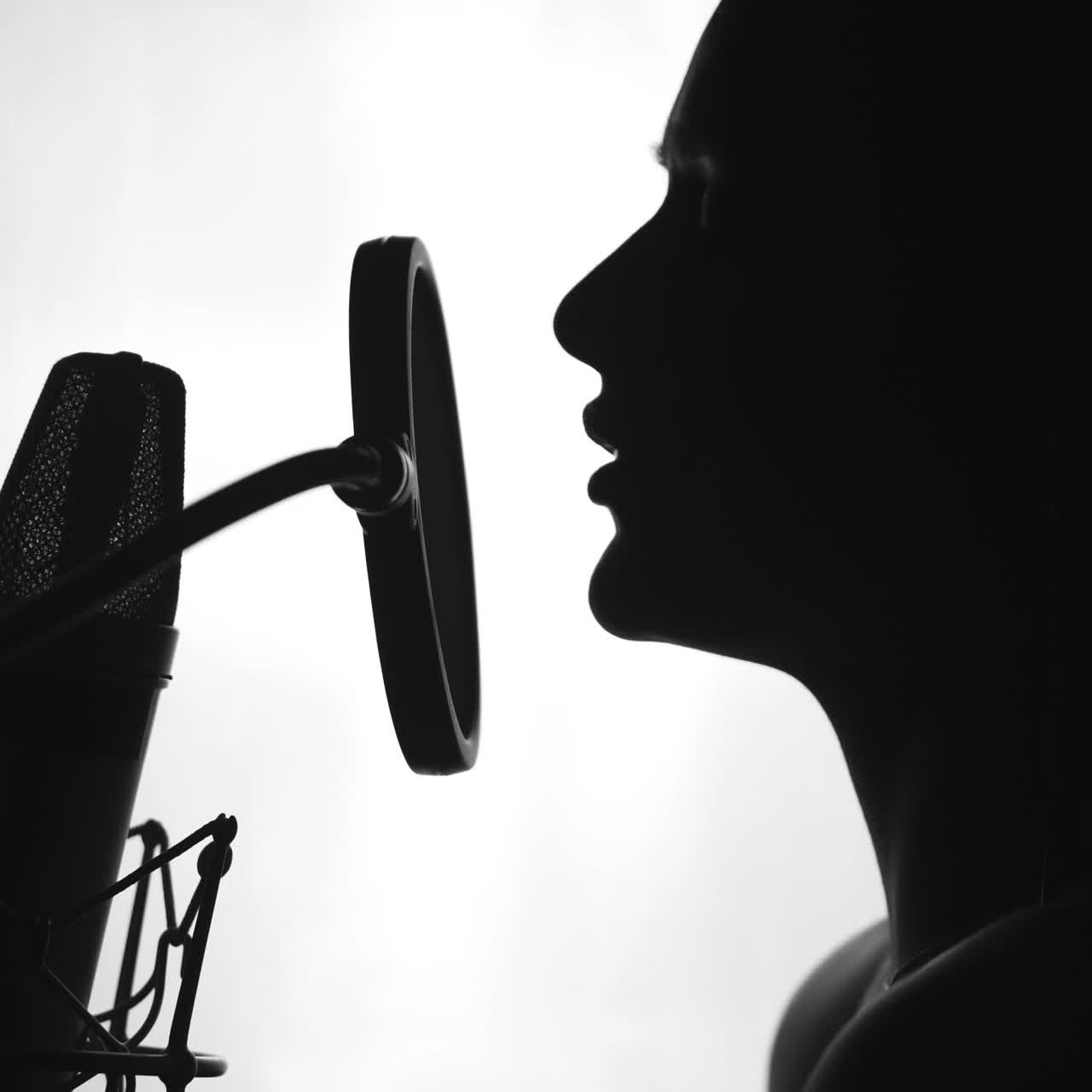 Young sexy profile of a woman with a beautiful face and lips. Girl singing to the microphone in a studio. Black and white Square video