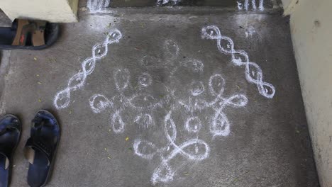 worn out rangoli in front of a household front door with shoes on the side