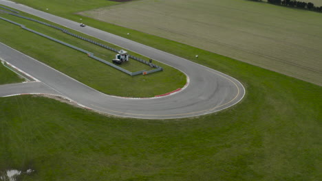 race car on a circuit taking a corner surrounded by green fields