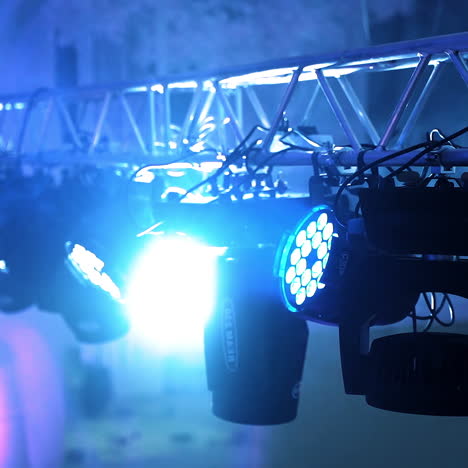 black projectors spinning and giving bright lights in the night club. metal construction and many spotlights hanging on it on the blue blurred background inside the hall.