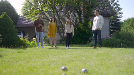 distant view of caucasian young woman throwing a petanque ball in the park on a sunny day while her friends waiting their turns