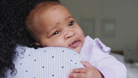 loving african american mother wearing pyjamas cuddling baby daughter in bedroom at home