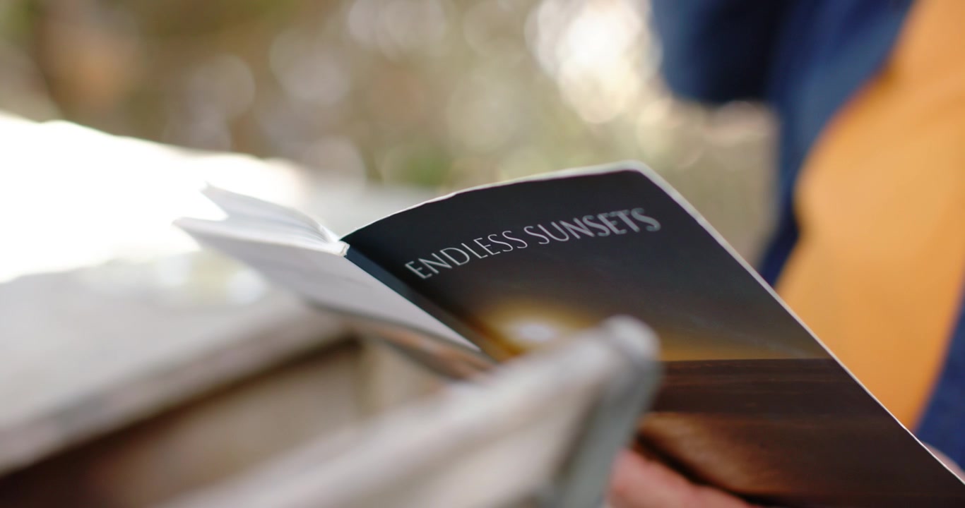 La mano destra inizia a sfogliare le pagine del libretto ENDLESS SUNSETS per rivelare il titolo sul portico vicino a una tazza.