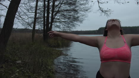 una mujer con un sostén deportivo rosa con los brazos abiertos mientras siente la belleza y la tranquilidad de la naturaleza - gran plano