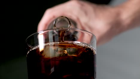 hand pouring coke or cola from a glass bottle into icy transparent drinking glass outdoors - closeup low angle view