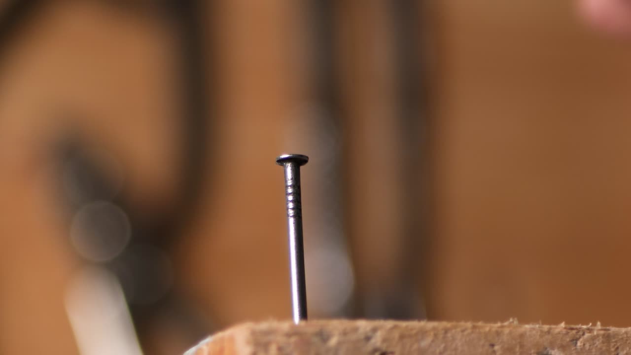 un primerísimo plano martillando un clavo en la madera con un martillo de metal, a cámara lenta