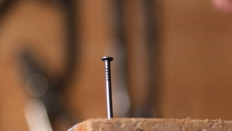 un primerísimo plano martillando un clavo en la madera con un martillo de metal, a cámara lenta