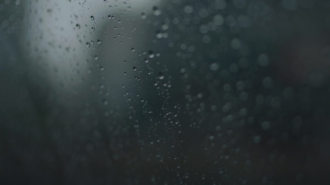 Macro shot capturing droplets of water on car window on rainy day.