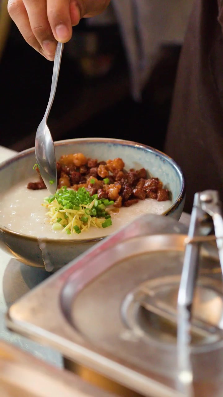 Close-up of a chef adding fresh scallions to a bowl of savory rice porridge.