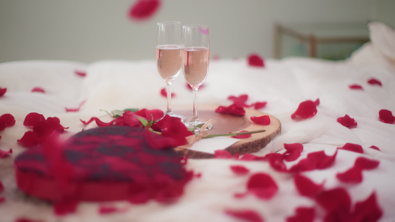Rose petals falling on Valentine's Day bedroom setting with wine, slow motion