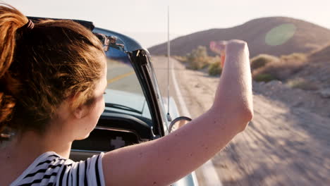 woman in the front passenger seat of open top car, back view