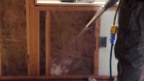 a worker fills in a small space with blown-in insulation