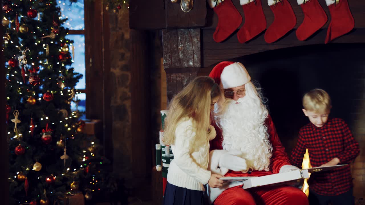 Santa Claus is showing an album with photos to kids on the background of a fireplace with Christmas socks and with a Christmas tree in the room, but the boy in a plaid shirt runs away.