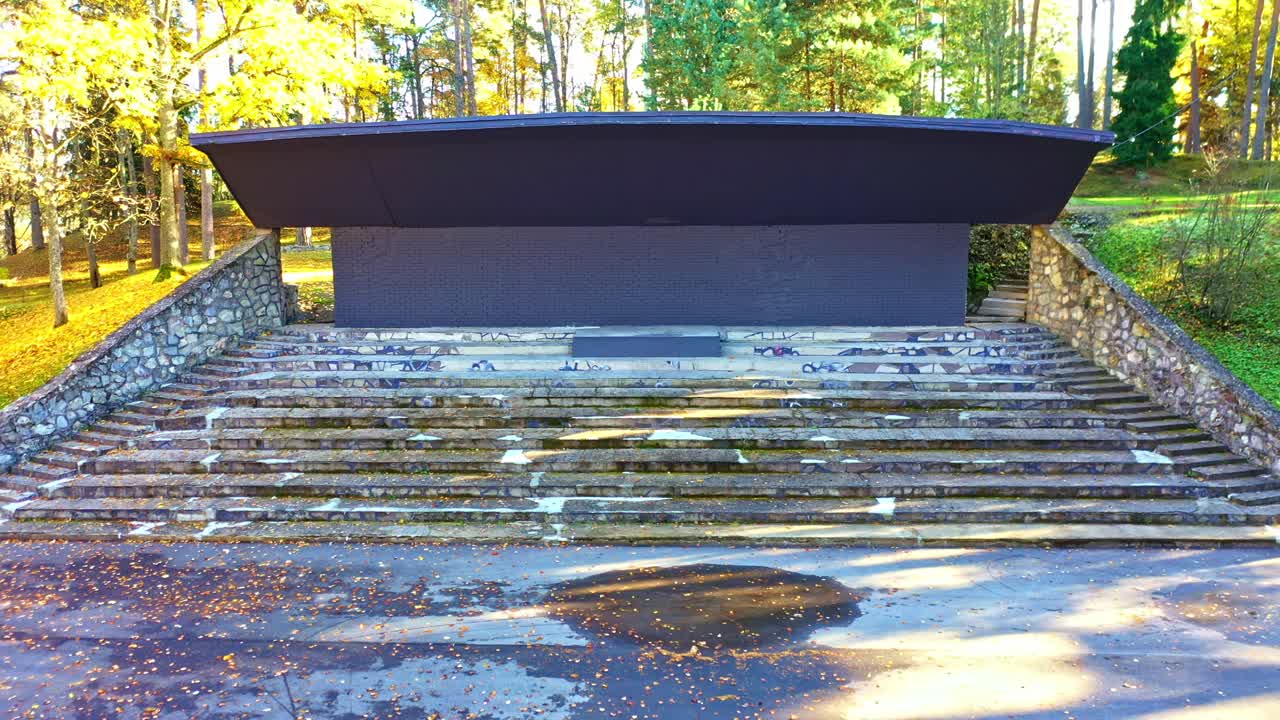 Outdoor concrete stage with stone walls and stairs in forest park setting, aerial view