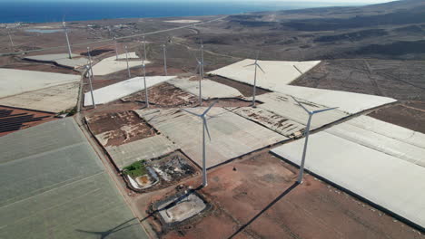 Volando-Sobre-Un-Campo-De-Turbinas-Eólicas-E-Invernaderos-En-Un-Paisaje-Desértico-En-La-Isla-De-Gran-Canaria-En-Un-Día-Soleado