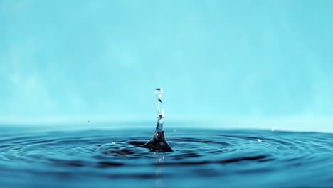 vídeo en 4k en cámara lenta de una superficie de agua con gotas que caen sobre un fondo azul. salpicaduras de agua. rodaje de estudio.