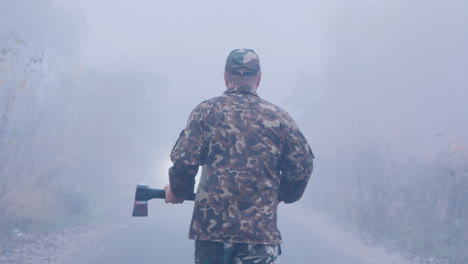 aggressive man with an ax is walking in the fog towards the car