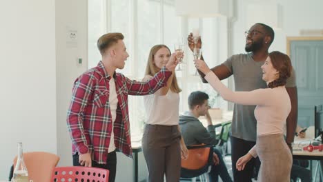 Gente-Feliz-Dando-Brindis-En-El-Espacio-De-Coworking.-Amigos-Sonrientes-Bebiendo-Juntos