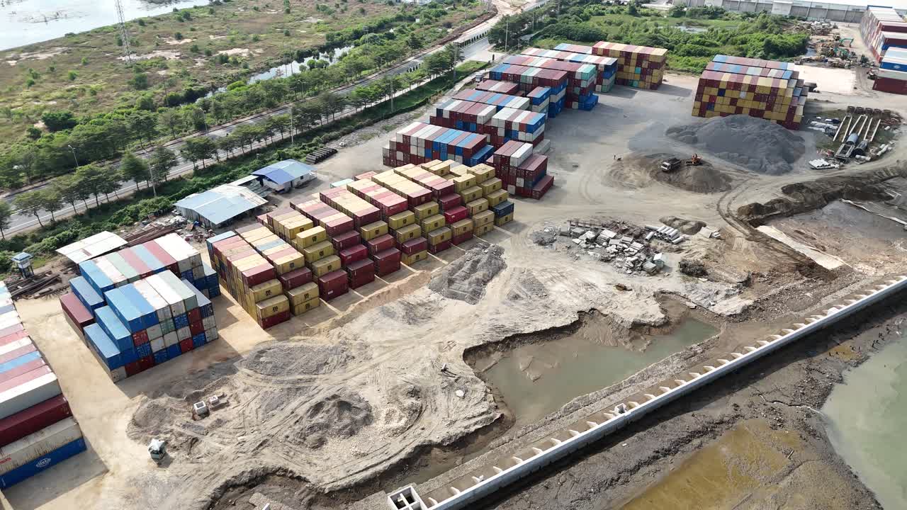 Drone footage captures a sprawling container yard in Vietnam, showcasing vibrant stacked containers amid industrial surroundings. Bright daylight illuminates the bustling, organized scene