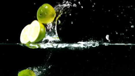 limas cayendo en el agua sobre un fondo negro