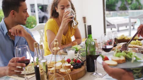 group of diverse male and female friends drinking wine and talking at dinner party on patio