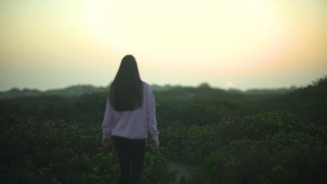 Wide-shot-of-a-girl-walking-in-nature-and-tying-up-her-hair-during-sunrise-or-sunset