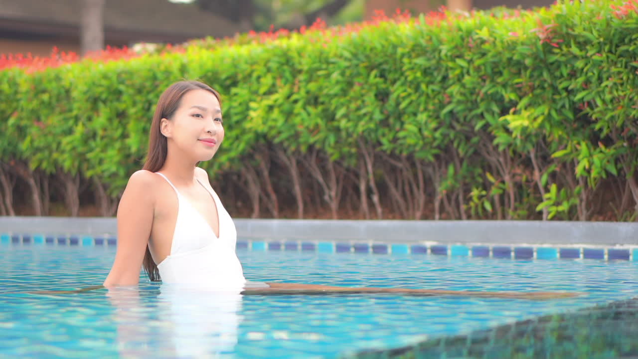 녹색 덤불 배경 - 휴가 개념에 미소 수영장 얕은 물 안에 앉아 휴식 흰색 수영복 여행자