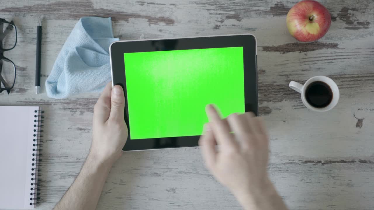 manos sosteniendo tableta pc con pantalla verde vacía en fondo de madera