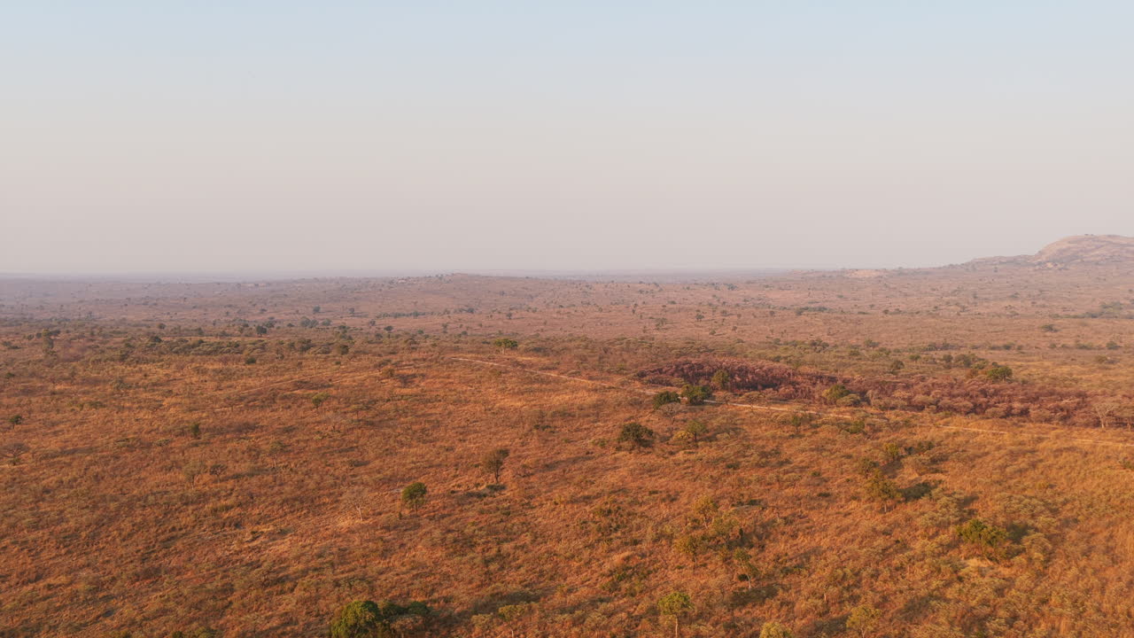 Golden-brown grasslands flow endlessly across the terrain, dotted with small shrubs and distant wildlife trails