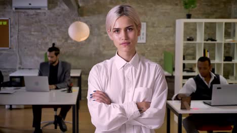 pretty businesswoman is standing and crossing her arms in office, colleagues are working with laptops, work concept