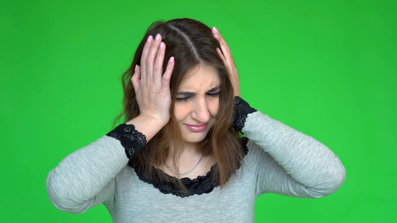 Portrait of beautiful young brunette touching her temples feeling stress, on green background.