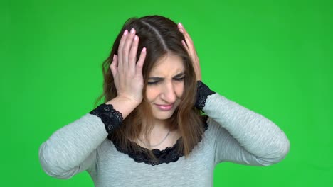 portrait of beautiful young brunette touching her temples feeling stress, on green background.