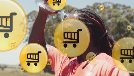 Animation-of-shopping-cart-icon-in-circles,-african-american-man-pouring-water-on-head